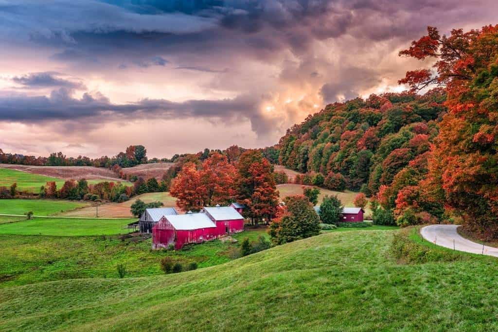 A backroad near a red farmhouse and barn and Vermont fall foliage. 