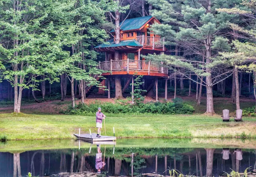 A man stands on a dock in the middle of a pond in front of a Vermont treehouse.