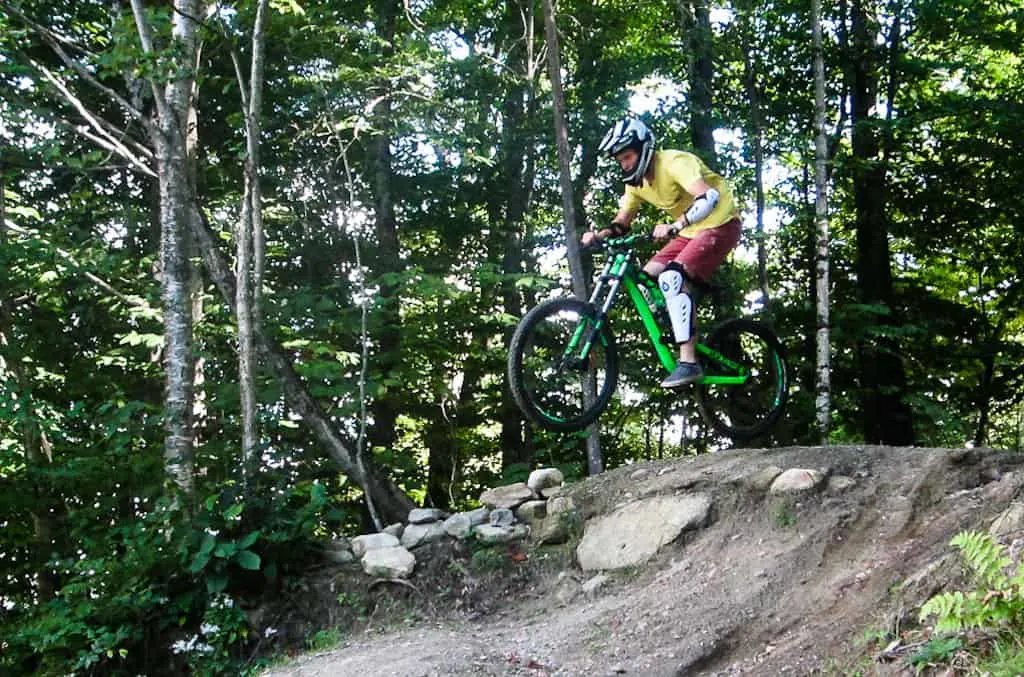 A teenager riding over a jump on the mountain bike trails at Mount Snow.