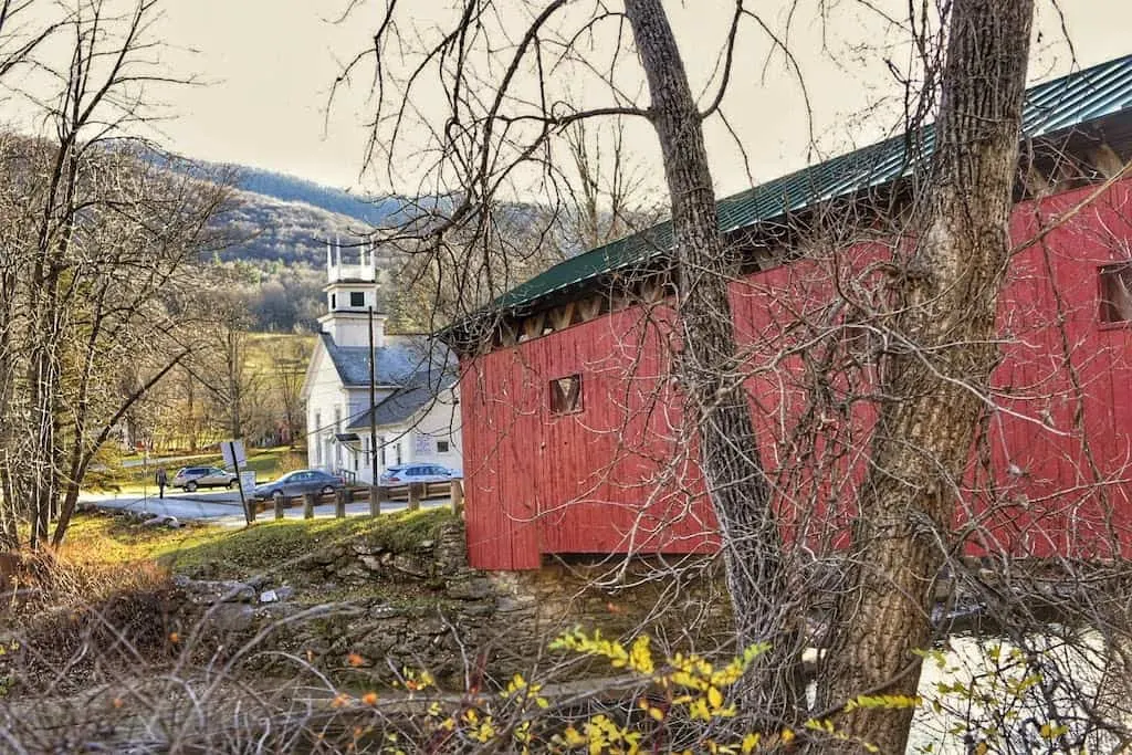 The Arlington Green Covered Bridge on a beautiful fall day in Vermont. You can see the historic church in the background.