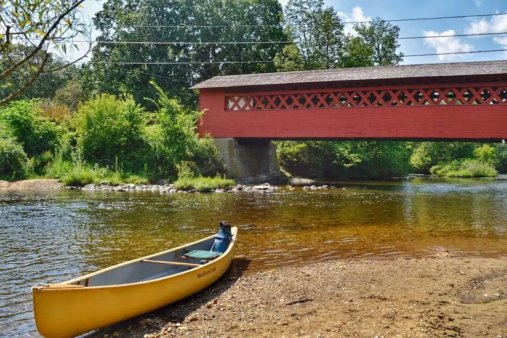 A yellow canoe is beached underneath the Burt Henry Covered Bridge in North Bennington, VT.