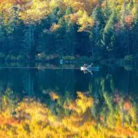 A fall foliage view of a canoe paddling the calm waters of Grout Pond in Vermont.