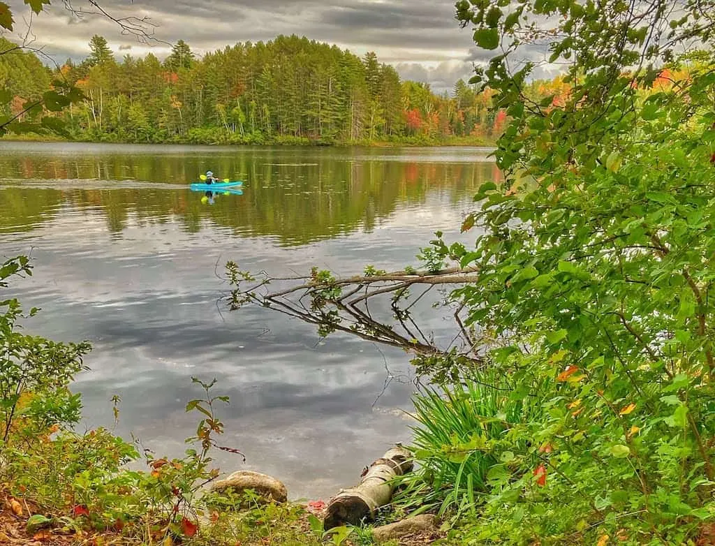 A woman paddles a canoe on Spectacle Pond in Brighton State Park, Vermont during the fall.