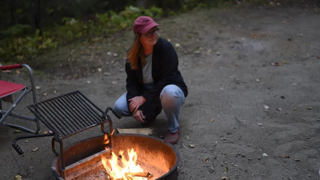 A woman sits next to a campfire in Vermont State Parks.