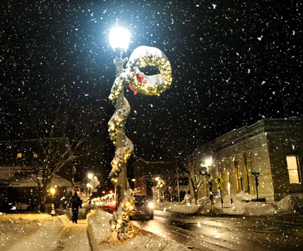 A wreath wrapped in Christmas Lights and surrounded by snow.