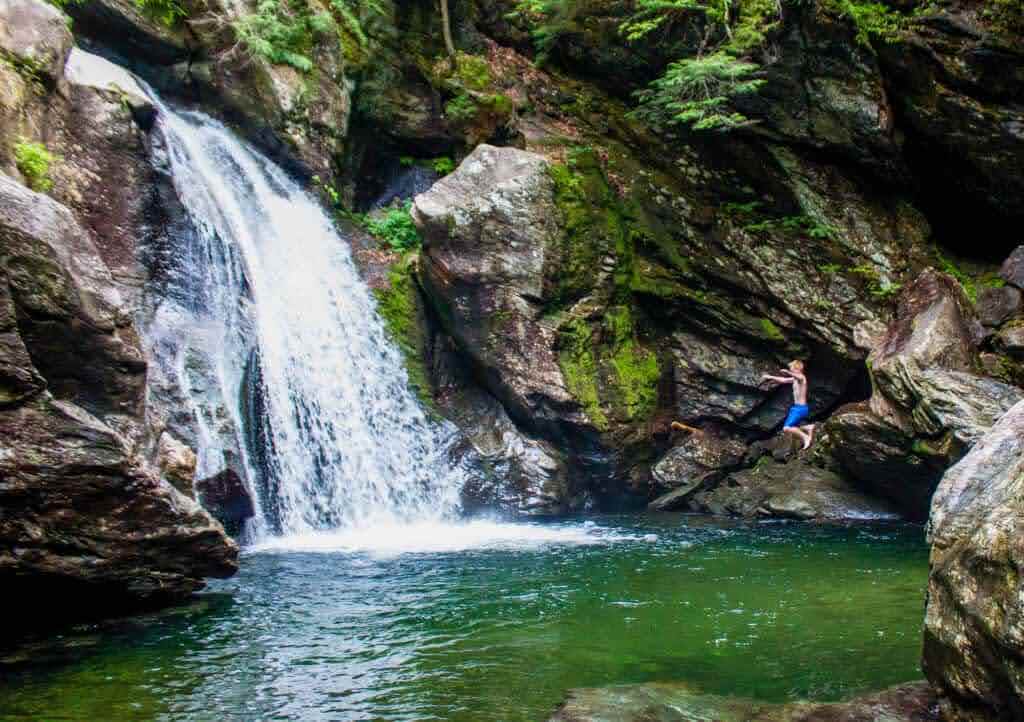 A young boy jumps off a cliff into a Vermont swimming hole at Bingham Falls in Stowe.