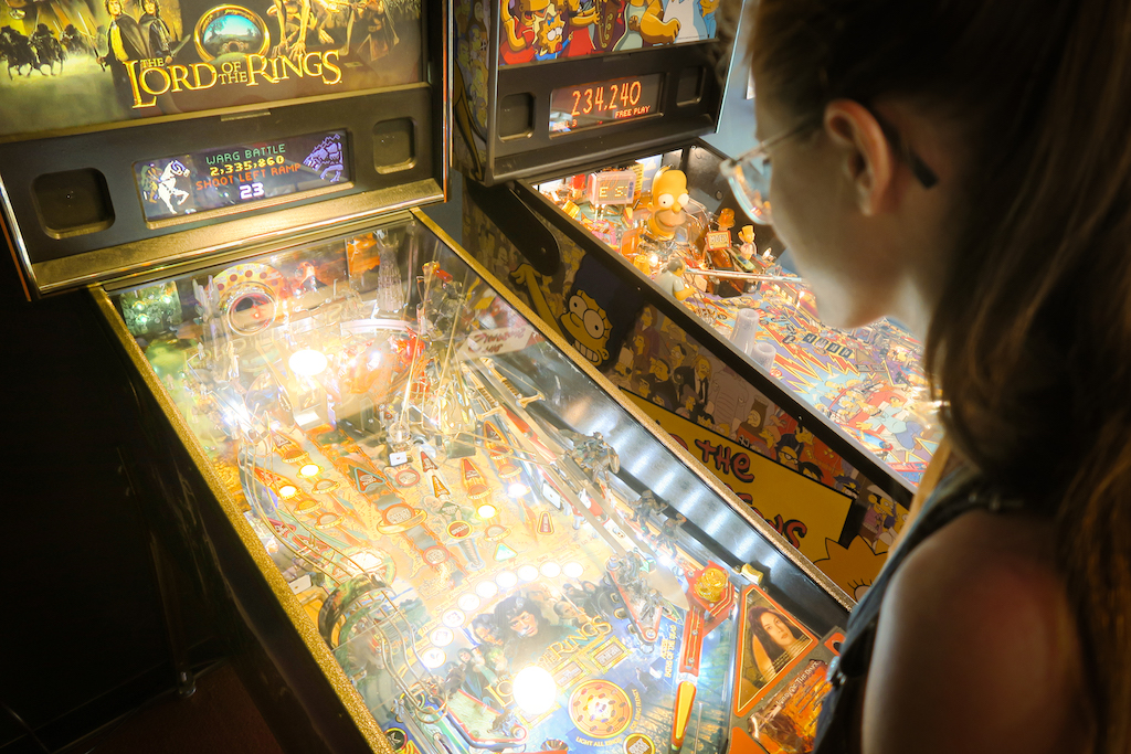 A woman leans over a pinball machine and the glow from it lights up her face.