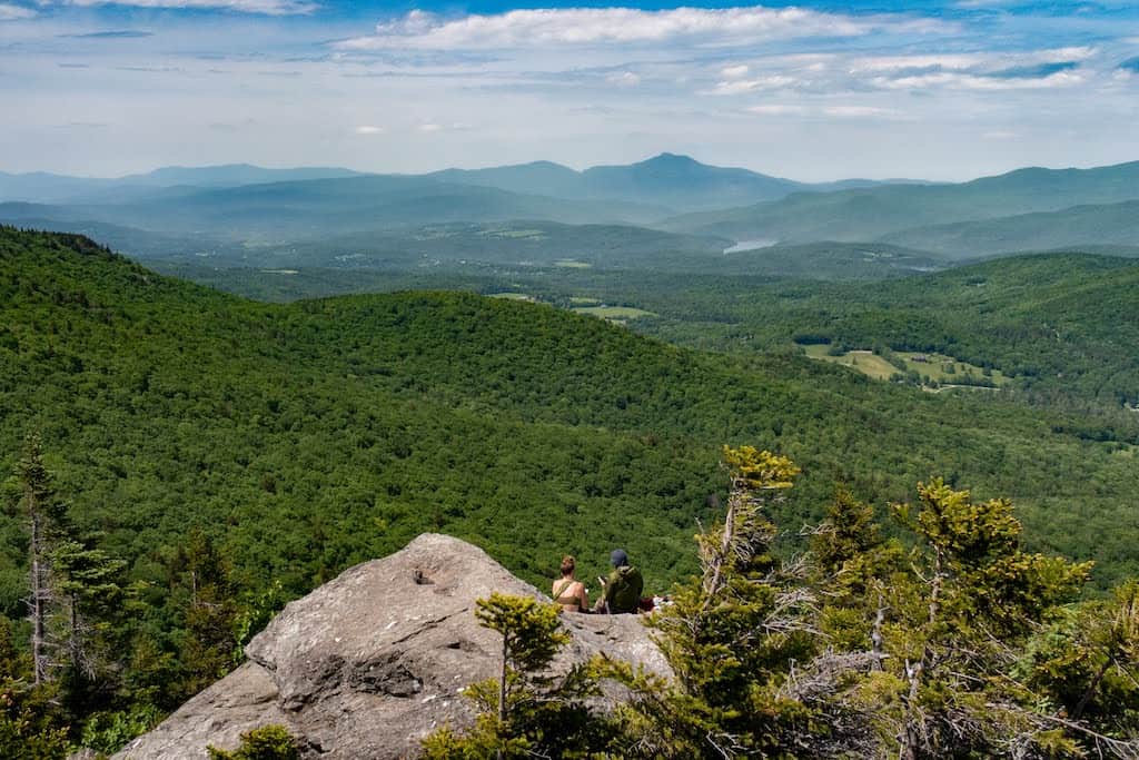 A couple sits on a knobby pinnacle after hiking in Stowe, Vermont.