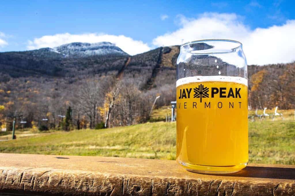 A glass of beer with the Jay Peak logo sitting on a railing in front of the lift line at Jay Peak in Vermont.