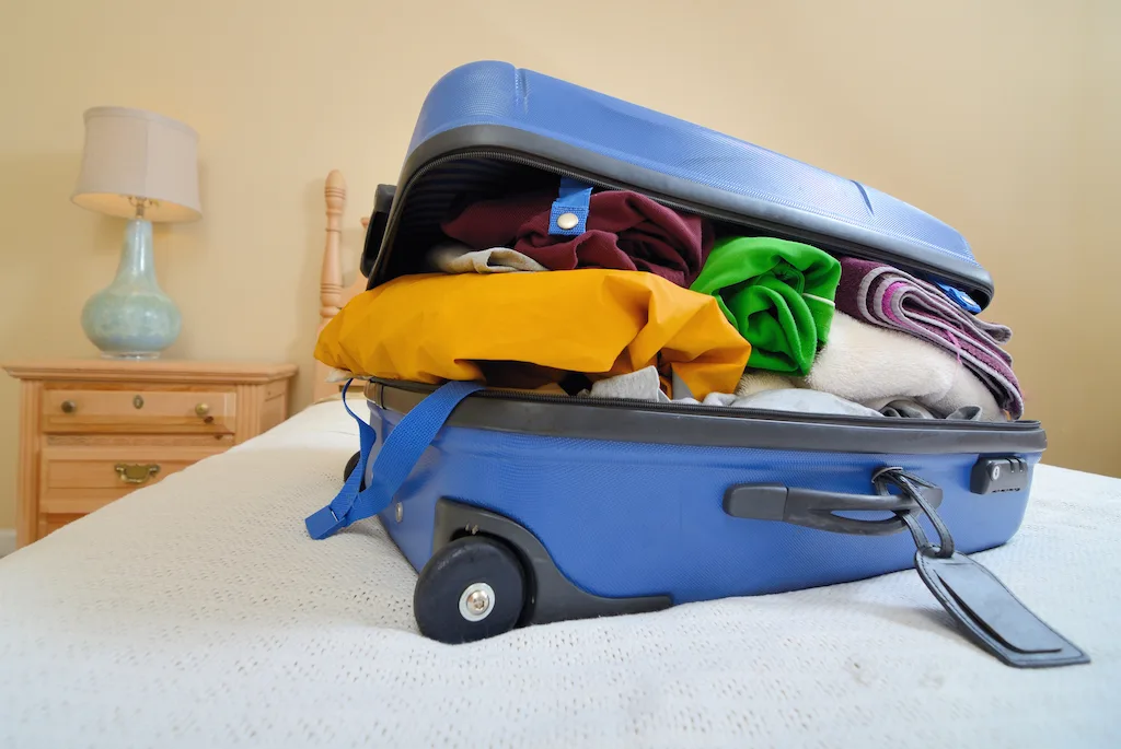 A stuffed carry-on suitcase on a bed.