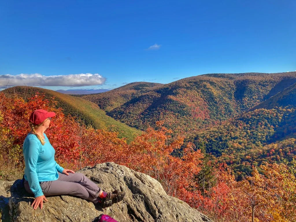 Tara sitting on a rock surrounded by mountains with beautiful fall foliage.