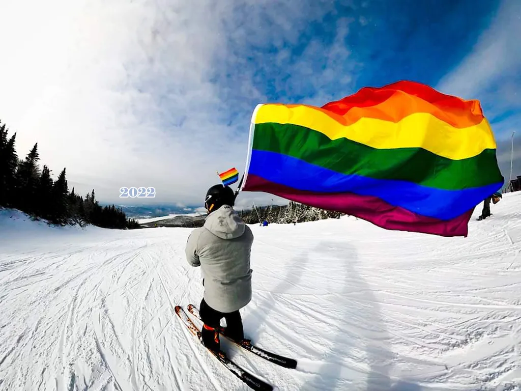 A man skiing with a colorful rainbow flag at Stowe Mountain Resort. 