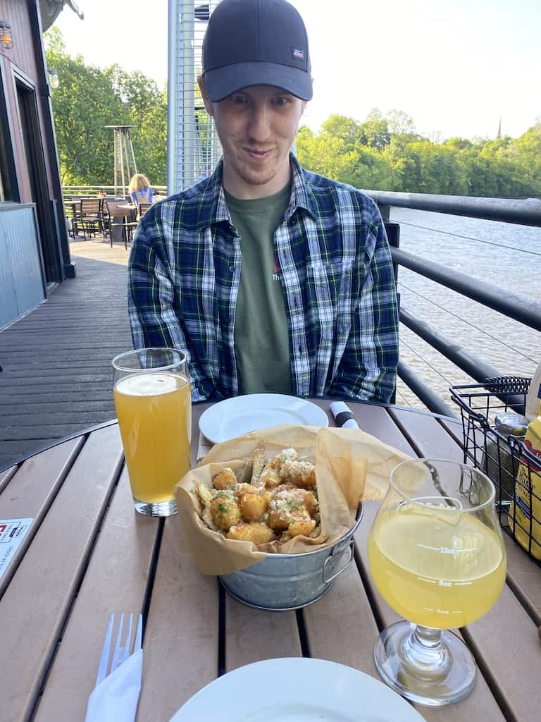 Gabe sits near the Connecticut River with a craft beer and pretzel bits from Whetstone Station.