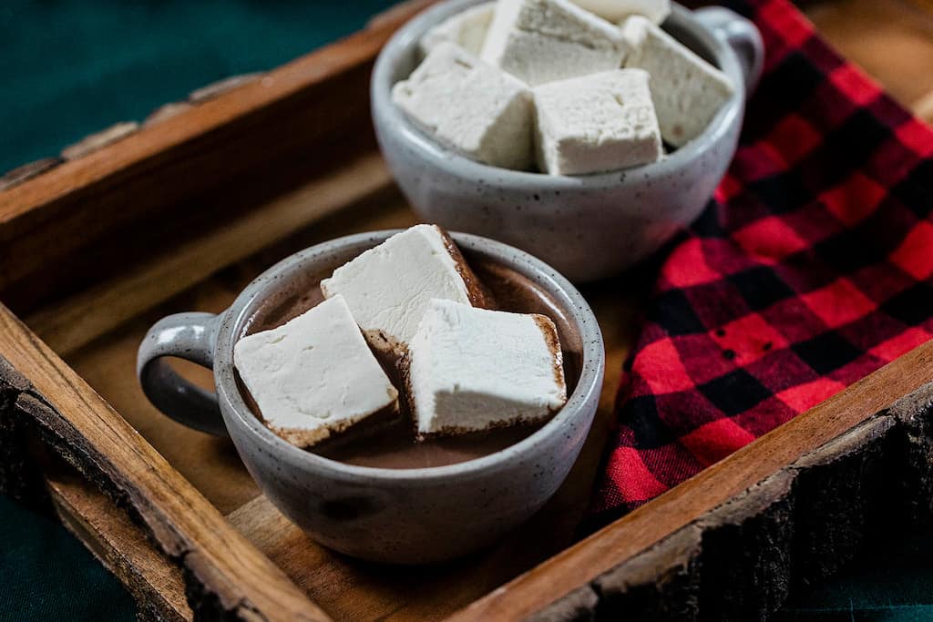 Vermont Marshmallows in two mugs of hot cocoa on a wooden tray.