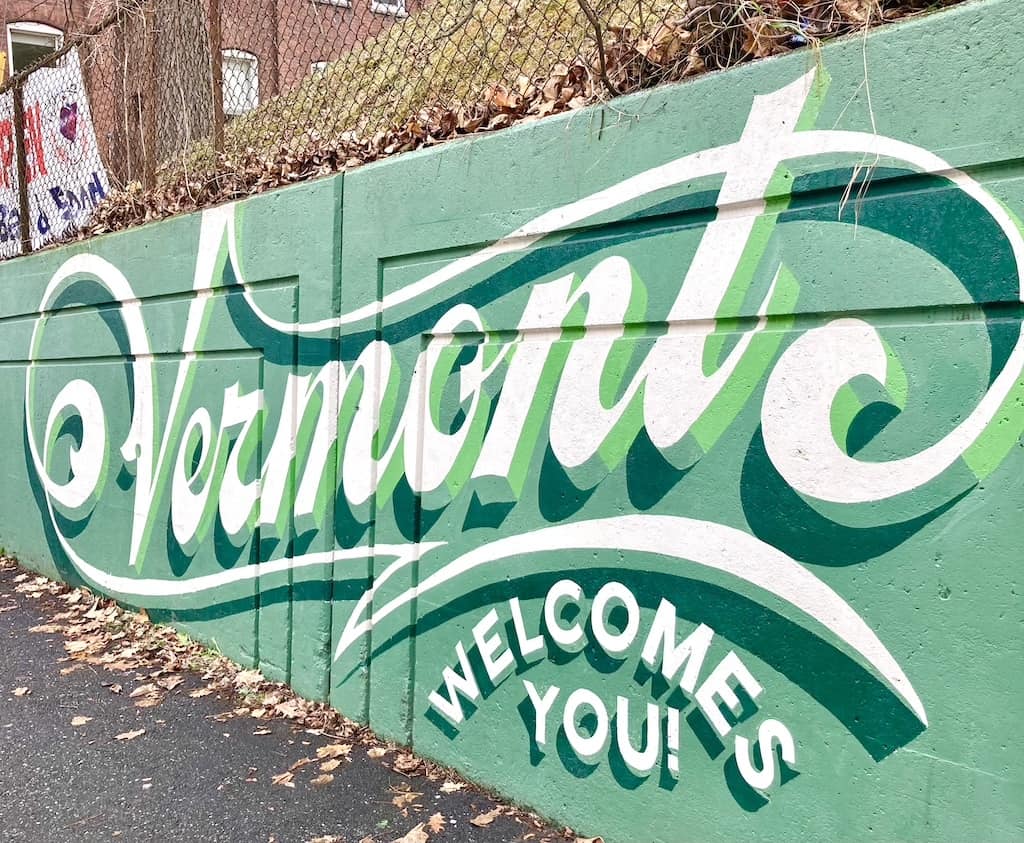A mural with writing in script on a green background that says 'Vermont Welcomes You'.