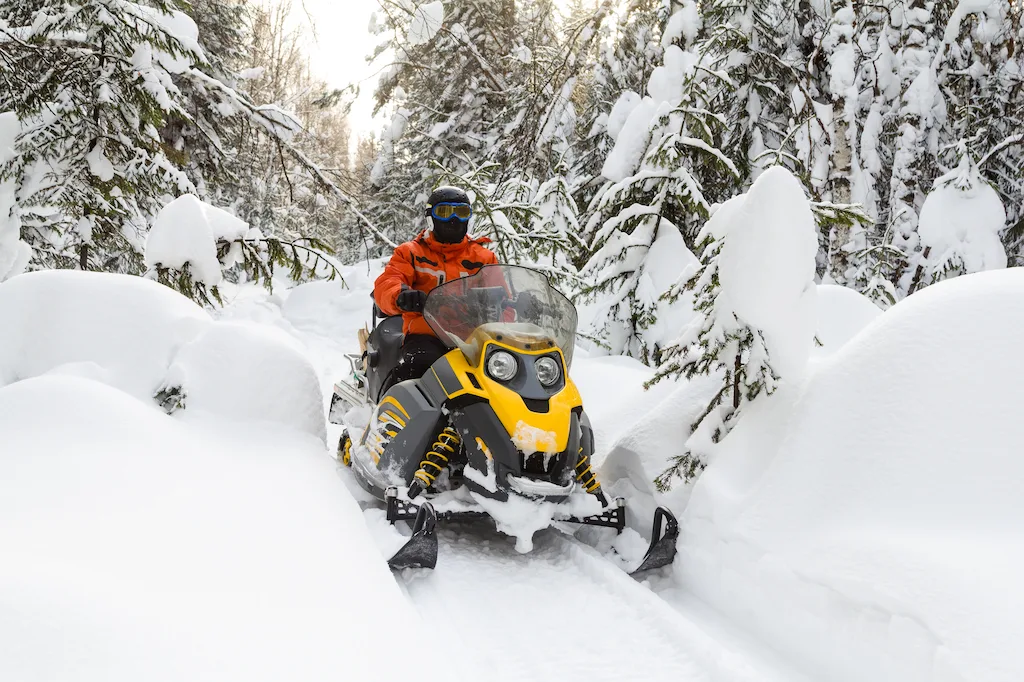 A man on a snowmobile in snow-covered woods of Vermont.