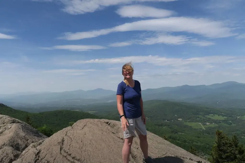 Tara standing at the top of Stowe Pinnacle on a windy summer day. 