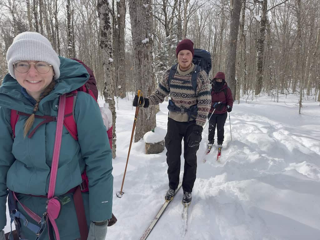 Three people skiing on a snowy trail toward Grout Pond Hut. 