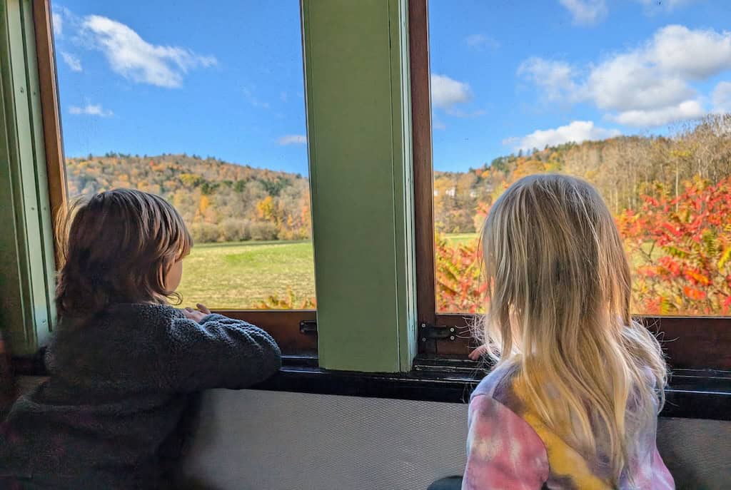 Two children looking out a train window at the fall foliage in St. Johnsbury.